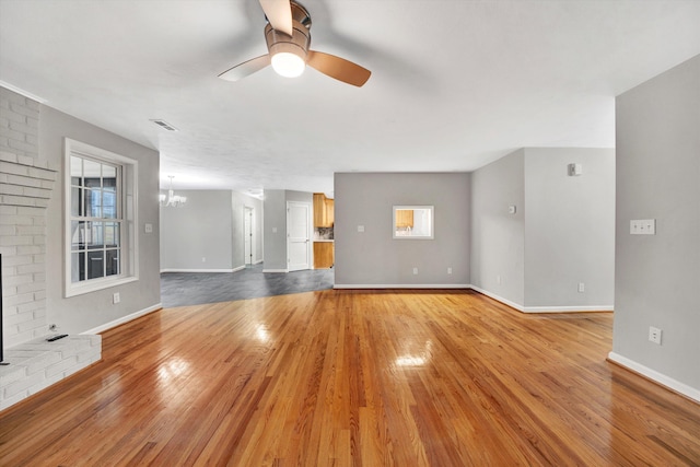 unfurnished living room featuring light wood-style floors, visible vents, baseboards, and ceiling fan with notable chandelier