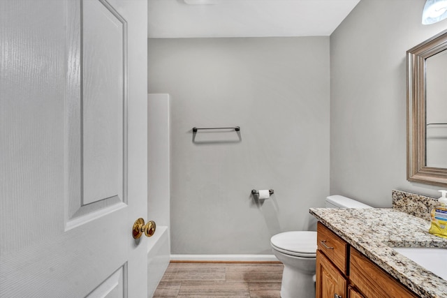 full bathroom with a tub to relax in, toilet, wood finished floors, vanity, and baseboards