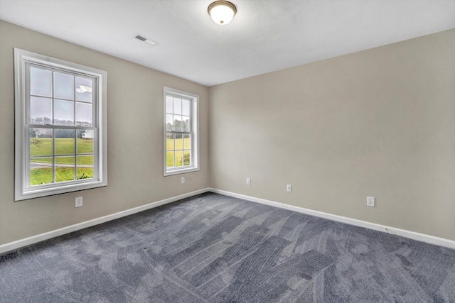 spare room with dark colored carpet, visible vents, and baseboards