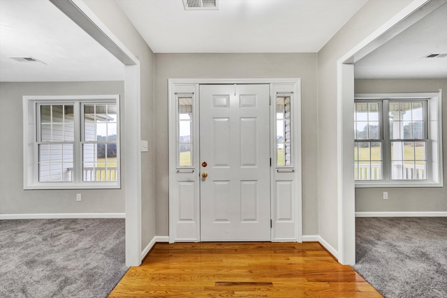 foyer with baseboards, visible vents, and light colored carpet