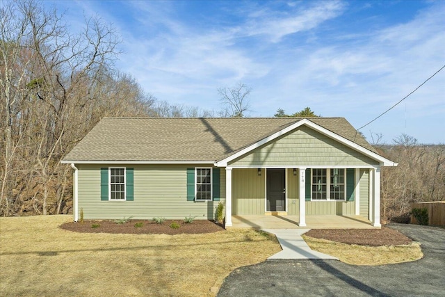 ranch-style home featuring covered porch, board and batten siding, a front yard, and roof with shingles