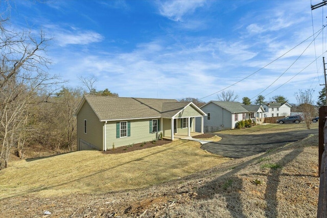 view of front of home with a front lawn, dirt driveway, and a shingled roof