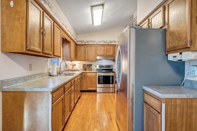 kitchen featuring lofted ceiling, appliances with stainless steel finishes, light wood-style floors, a sink, and under cabinet range hood