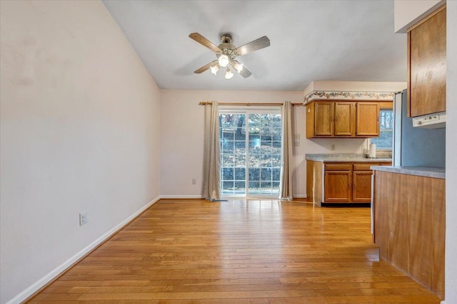 kitchen with brown cabinets, light countertops, light wood-style flooring, ceiling fan, and baseboards