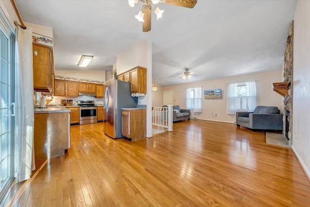 kitchen featuring stainless steel appliances, light wood-type flooring, open floor plan, and brown cabinetry