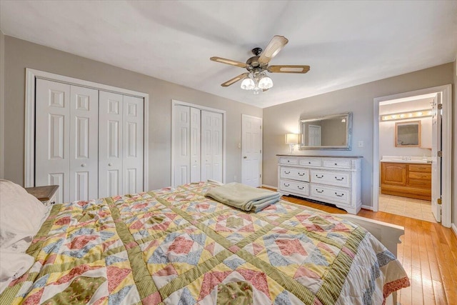 bedroom with light wood finished floors, ensuite bath, a ceiling fan, and two closets