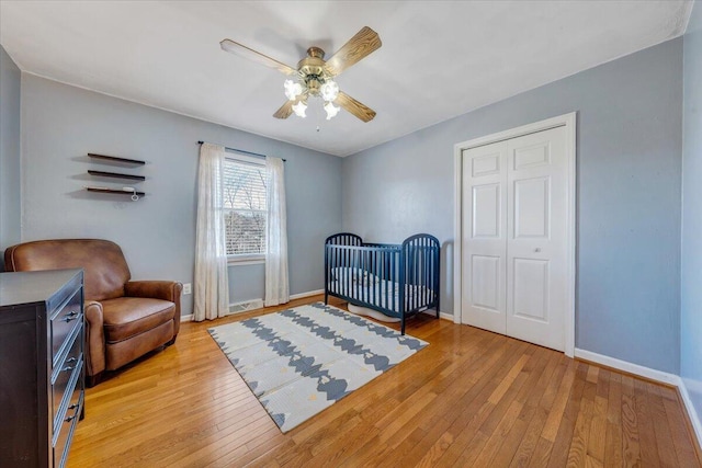 bedroom with light wood finished floors, a nursery area, baseboards, and a ceiling fan