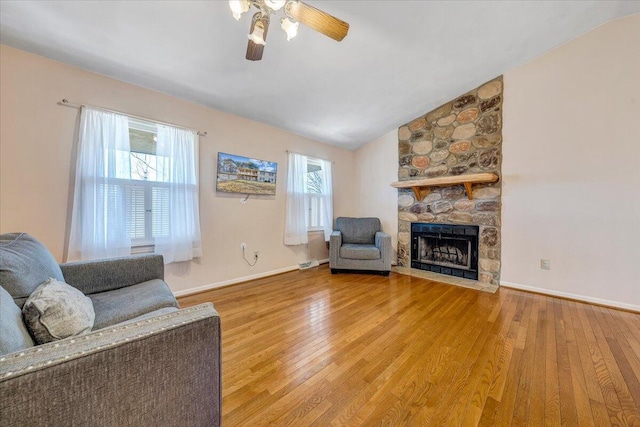 living area featuring ceiling fan, a fireplace, baseboards, vaulted ceiling, and light wood-type flooring