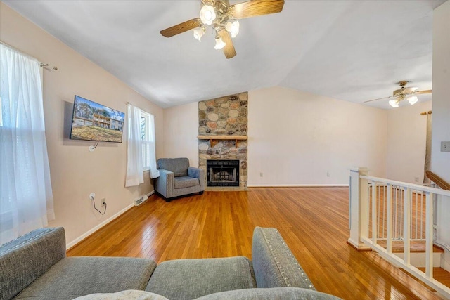 living area with lofted ceiling, wood-type flooring, a ceiling fan, a stone fireplace, and baseboards