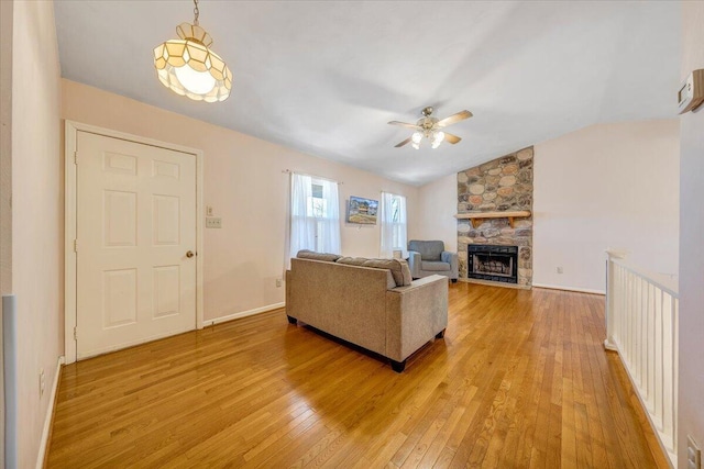 living area featuring lofted ceiling, light wood-style flooring, a fireplace, a ceiling fan, and baseboards