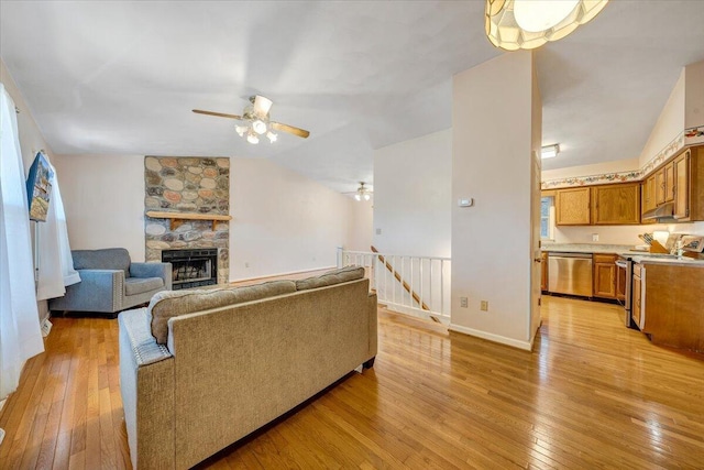 living room featuring light wood finished floors, baseboards, a ceiling fan, vaulted ceiling, and a fireplace