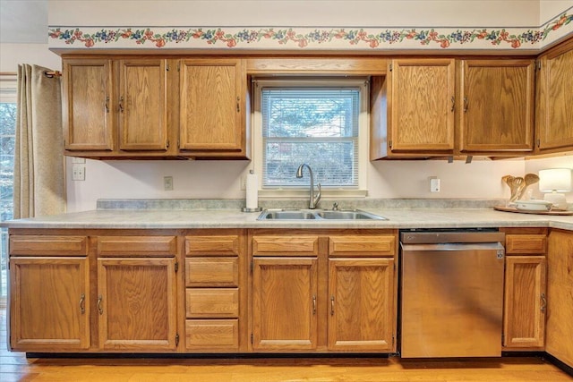 kitchen with brown cabinets, light countertops, a sink, and stainless steel dishwasher