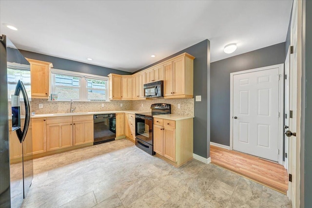 kitchen with light countertops, light brown cabinets, black appliances, and a sink