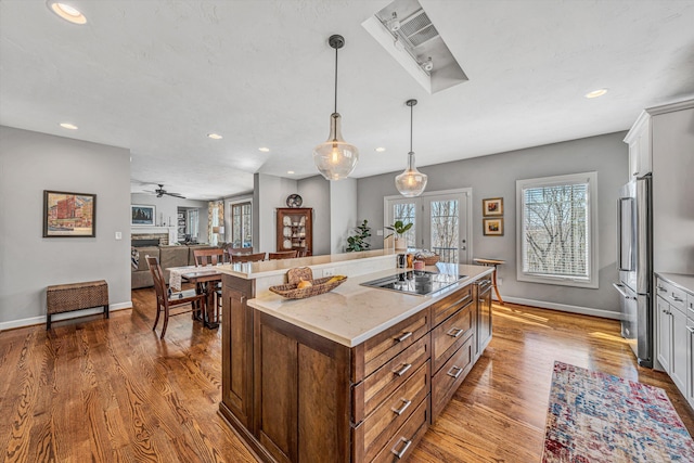 kitchen featuring a stone fireplace, black electric cooktop, high end refrigerator, wood finished floors, and a center island