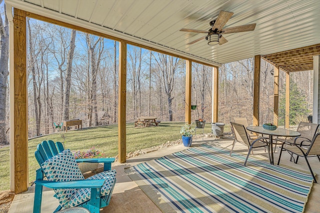 unfurnished sunroom featuring a forest view and a ceiling fan