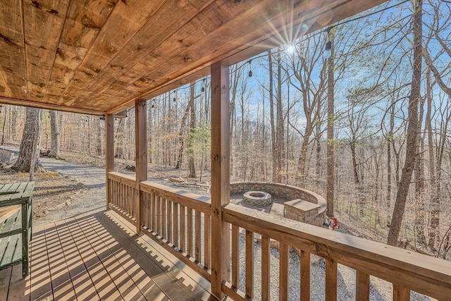 wooden deck featuring an outdoor fire pit and a view of trees