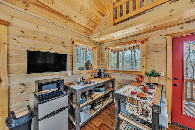 kitchen featuring wooden walls, black microwave, vaulted ceiling, and refrigerator