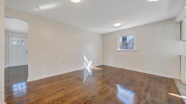 empty room featuring visible vents, baseboards, and dark wood finished floors