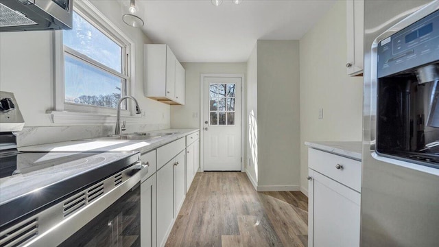 kitchen with light wood finished floors, electric range, light stone countertops, white cabinetry, and a sink