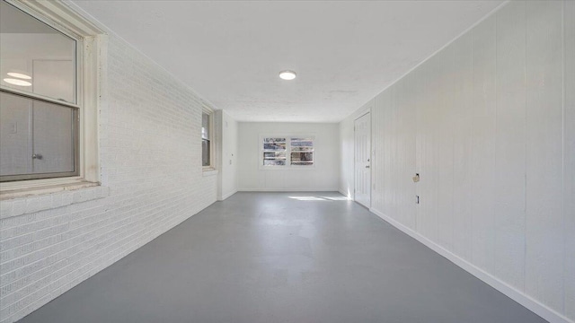 empty room featuring finished concrete flooring, brick wall, and baseboards