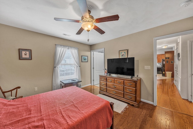 bedroom with a ceiling fan, visible vents, baseboards, and wood finished floors