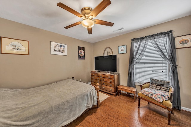 bedroom featuring a ceiling fan, visible vents, baseboards, and wood finished floors