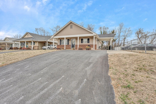 view of front facade featuring driveway, an attached carport, covered porch, fence, and brick siding