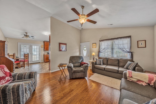 living area with lofted ceiling, visible vents, a ceiling fan, light wood-type flooring, and baseboards