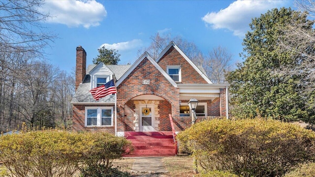 english style home with brick siding and a chimney