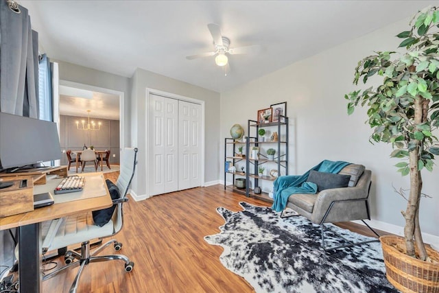 office space featuring baseboards, wood finished floors, and ceiling fan with notable chandelier