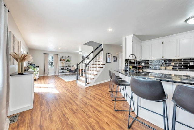 kitchen with tasteful backsplash, dark countertops, light wood-style flooring, a breakfast bar, and white cabinetry