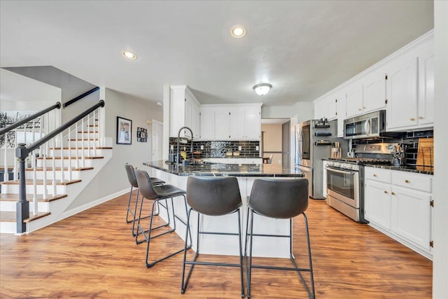 kitchen with a peninsula, appliances with stainless steel finishes, light wood-style flooring, and white cabinetry