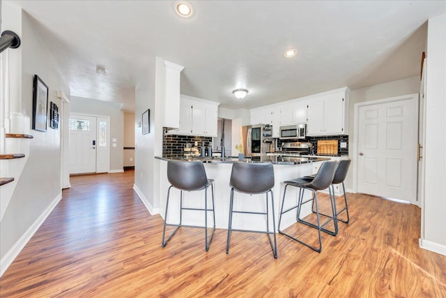 kitchen with a peninsula, dark countertops, stainless steel microwave, and a breakfast bar area