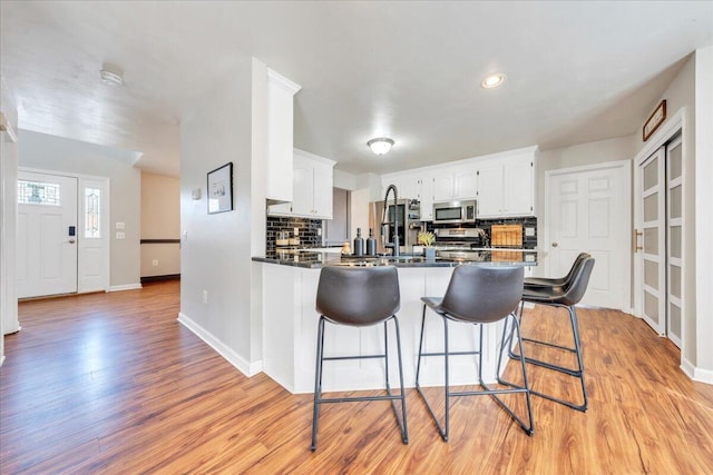 kitchen with a breakfast bar area, stainless steel appliances, backsplash, light wood-style floors, and a peninsula