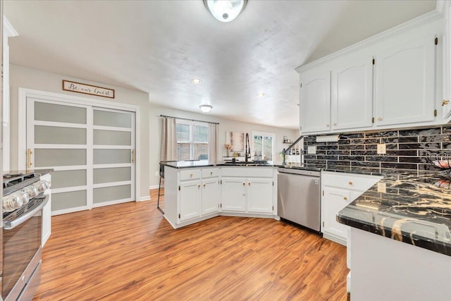 kitchen featuring light wood finished floors, dark countertops, appliances with stainless steel finishes, a peninsula, and a sink