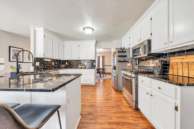 kitchen featuring stainless steel appliances, decorative backsplash, a sink, light wood-type flooring, and a peninsula