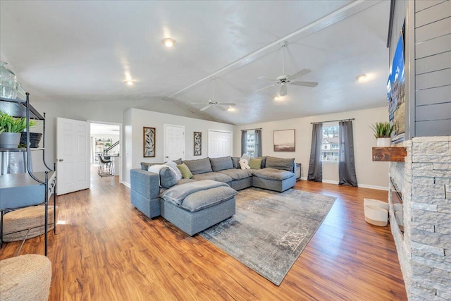 living area with lofted ceiling, a fireplace, wood finished floors, a ceiling fan, and baseboards