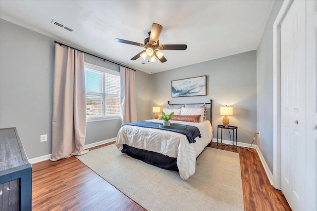 bedroom with a ceiling fan, wood finished floors, visible vents, and baseboards