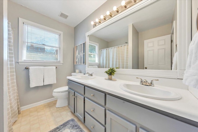 bathroom featuring toilet, double vanity, visible vents, and a sink