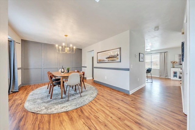 dining room featuring baseboards, light wood finished floors, an inviting chandelier, and a decorative wall