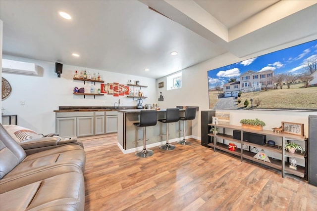 living area featuring indoor wet bar, recessed lighting, light wood-type flooring, a wall mounted air conditioner, and baseboards