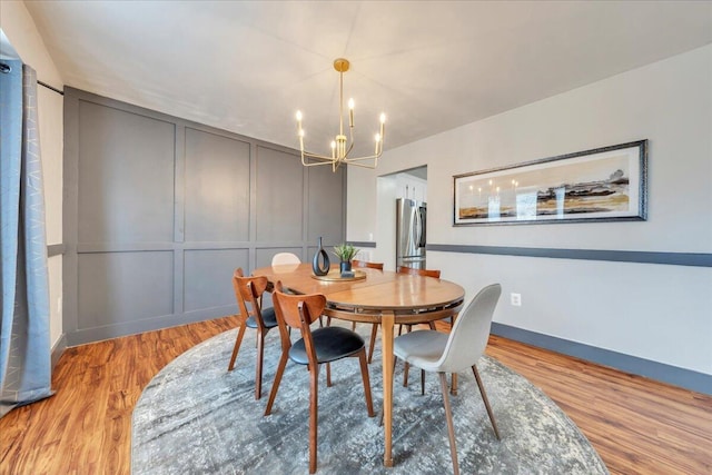 dining room featuring light wood-type flooring, an inviting chandelier, baseboards, and a decorative wall