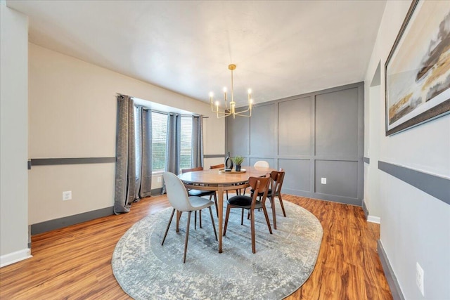 dining space featuring light wood-style floors, baseboards, a decorative wall, and an inviting chandelier