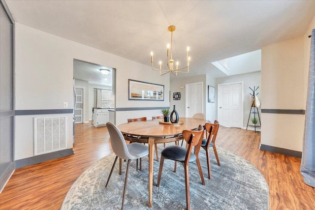 dining room with baseboards, wood finished floors, visible vents, and an inviting chandelier