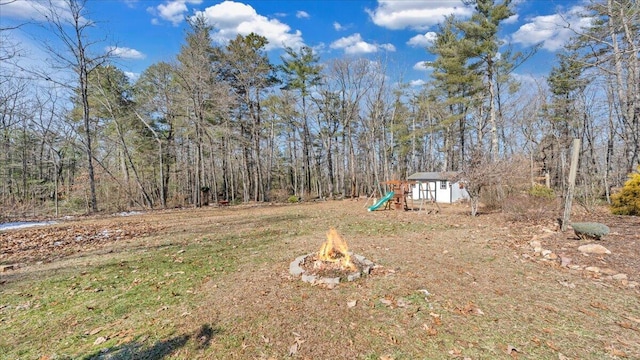 view of yard featuring an outbuilding, a playground, a fire pit, a shed, and a view of trees