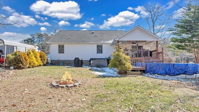 rear view of property featuring ceiling fan, an outdoor fire pit, a yard, a wooden deck, and a covered pool