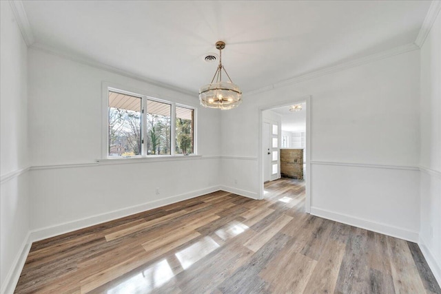 unfurnished dining area featuring baseboards, an inviting chandelier, wood finished floors, and crown molding