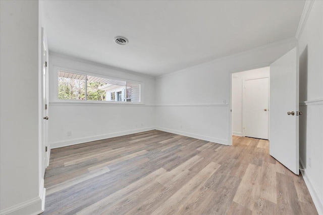 empty room with light wood-type flooring, visible vents, baseboards, and crown molding