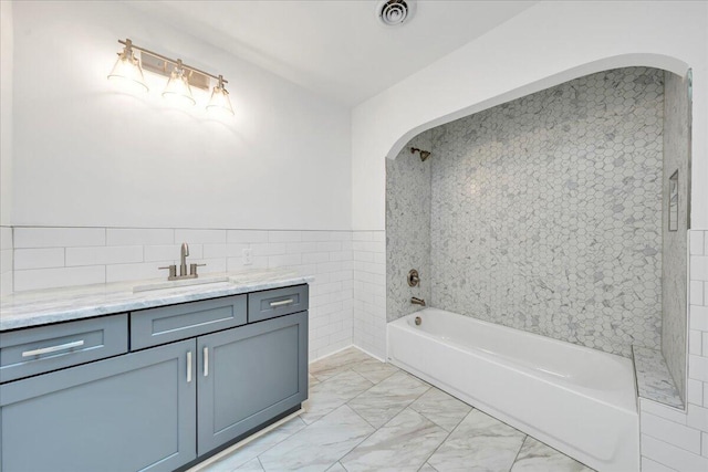 full bathroom with visible vents, vanity, bathtub / shower combination, marble finish floor, and tile walls