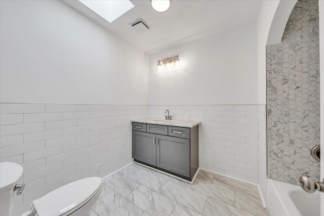 bathroom featuring visible vents, tile walls, toilet, a skylight, and vanity